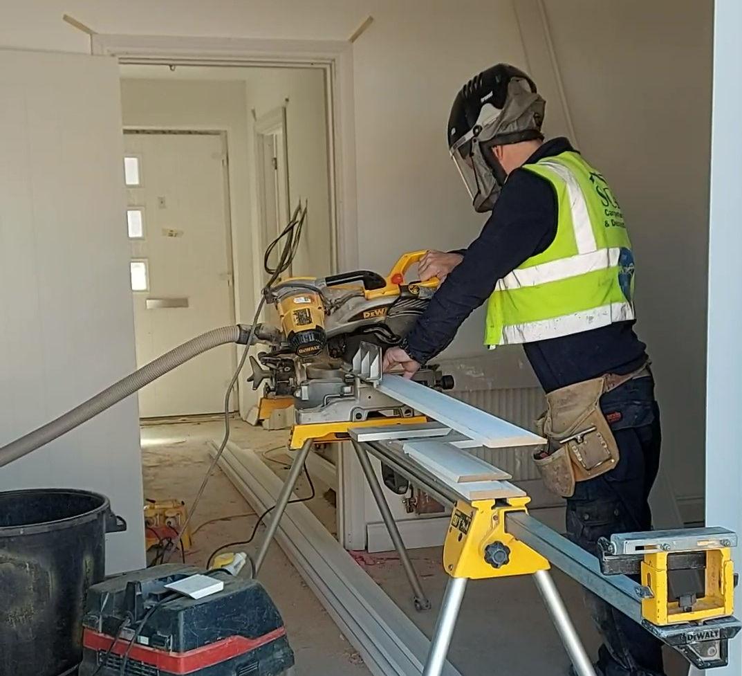 Carpenter in high-vis cutting architrave on a DeWalt mitre saw during a residential fit-out