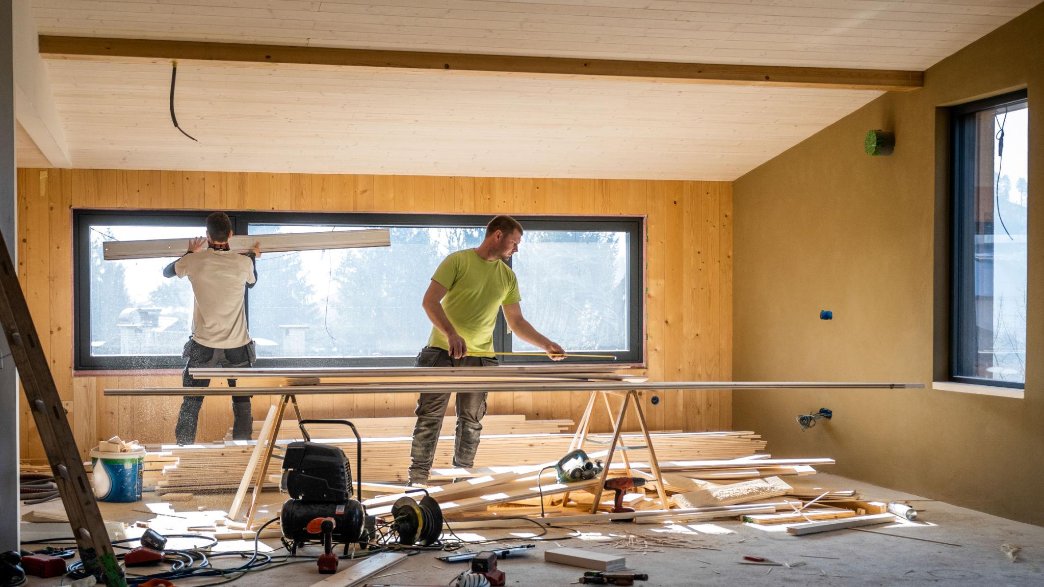 Two operatives measuring and fitting window linings in a timber-lined room