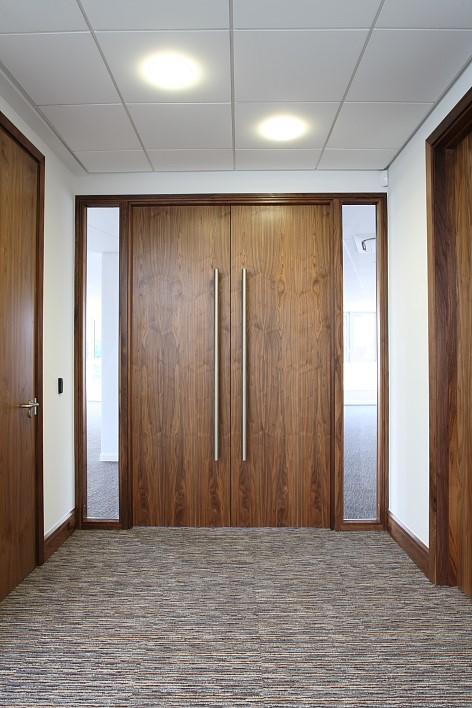 Finished commercial corridor with full-height walnut veneer double doors and suspended ceiling