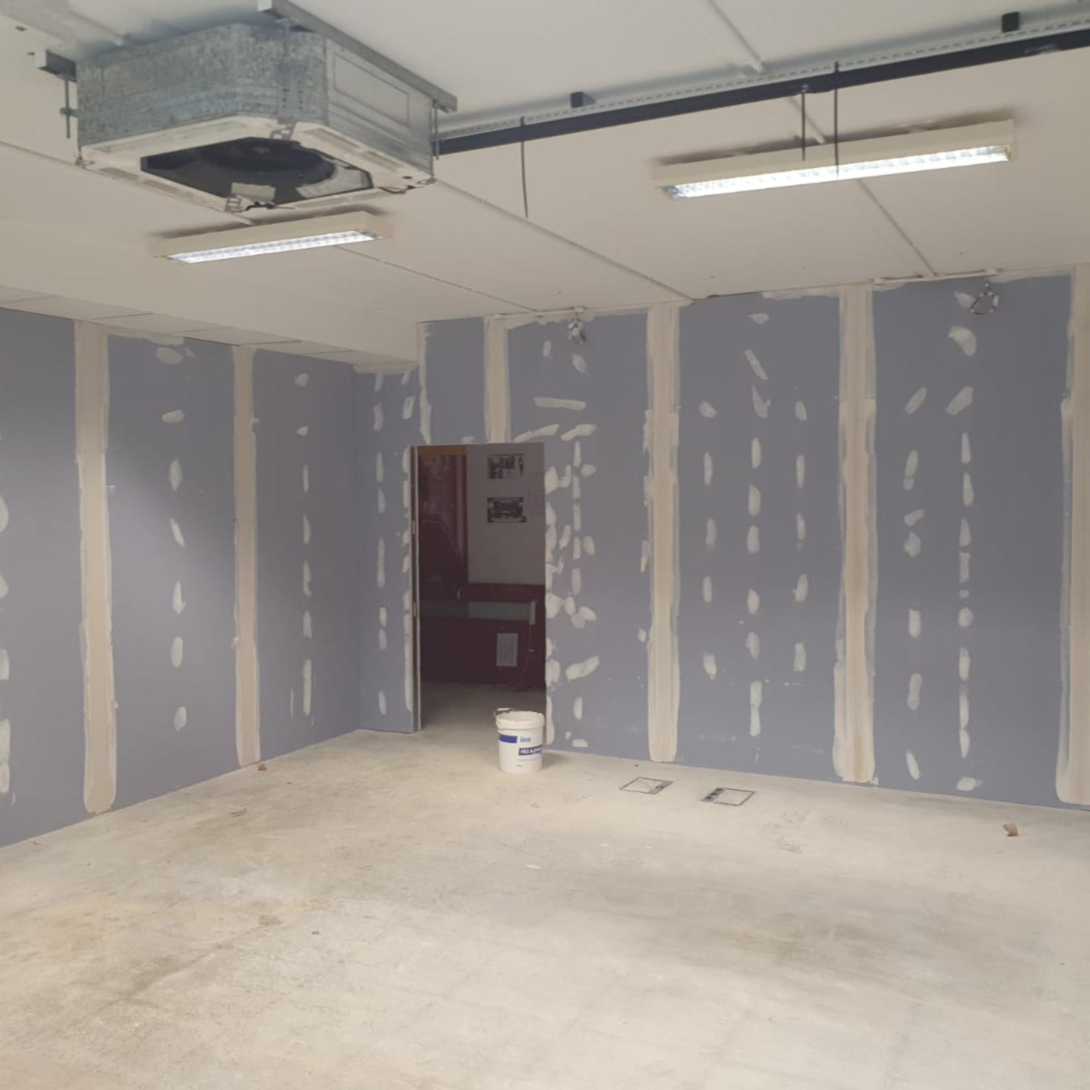 Completed drylining — commercial room with plasterboard walls taped and filled, suspended ceiling with HVAC unit