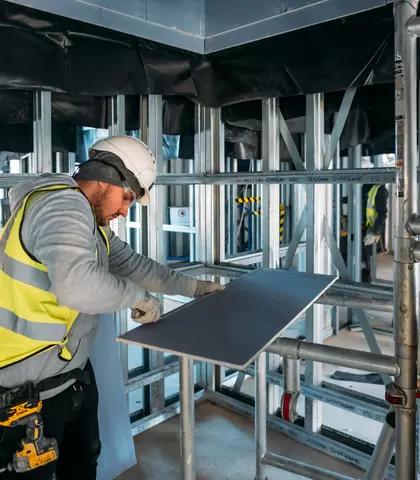 Operative fitting plasterboard sheet to metal stud framing on a large commercial site
