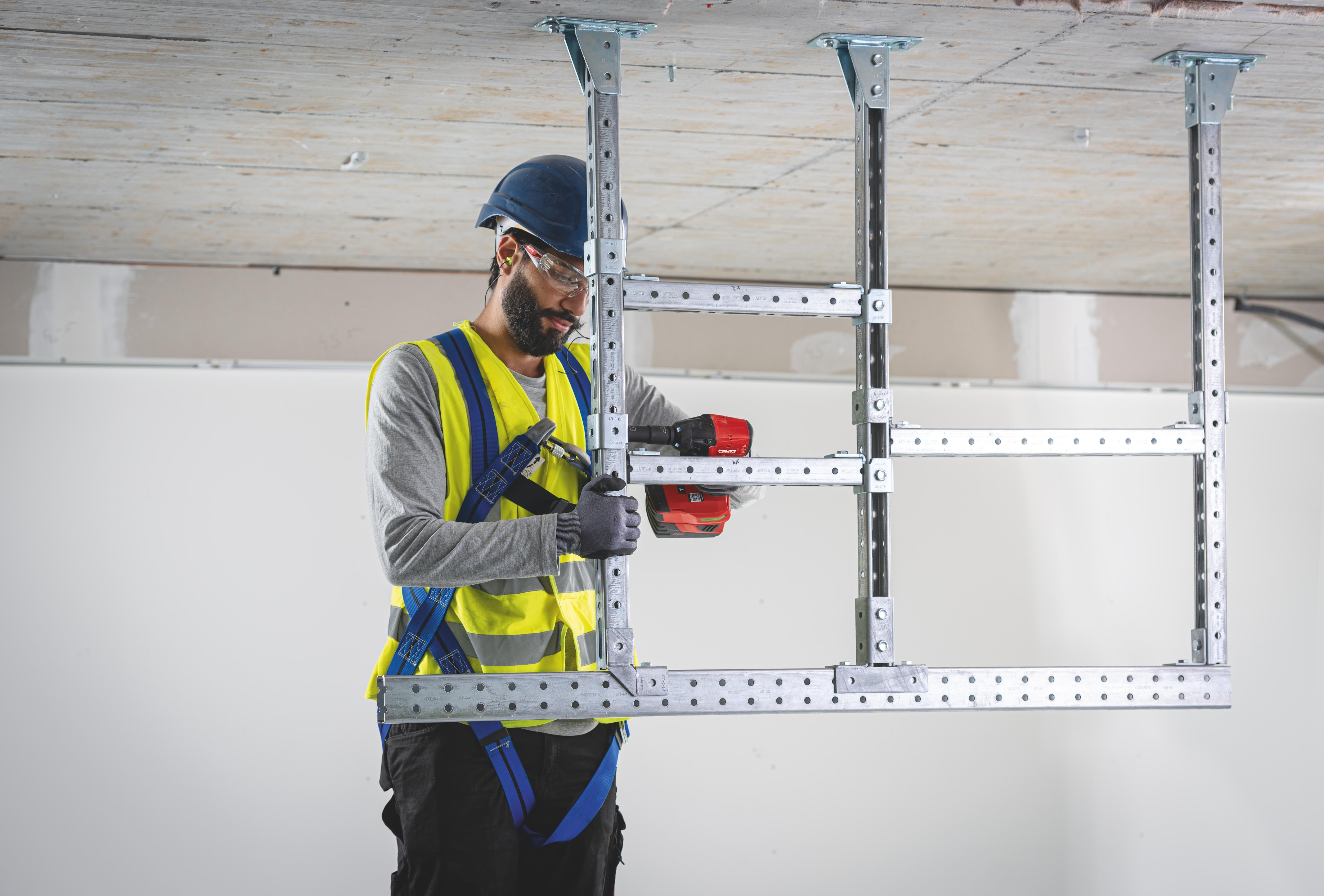 Operative assembling a metal stud frame section with a drill in an industrial setting