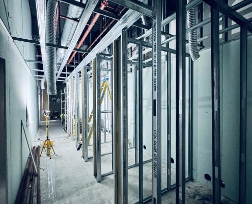 Commercial corridor showing metal stud partitions in progress with services and laser level — Takeair Ltd drylining London