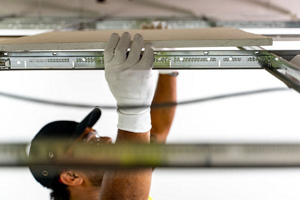 Operative's hands lowering a ceiling panel into a metal suspension grid