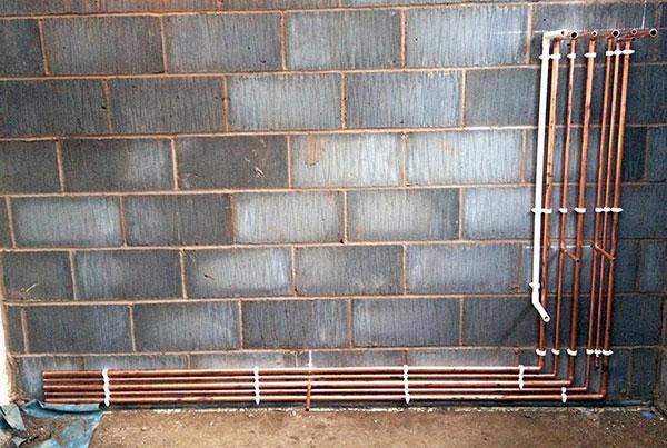 Neat copper first fix pipework on a block wall — horizontal and vertical runs