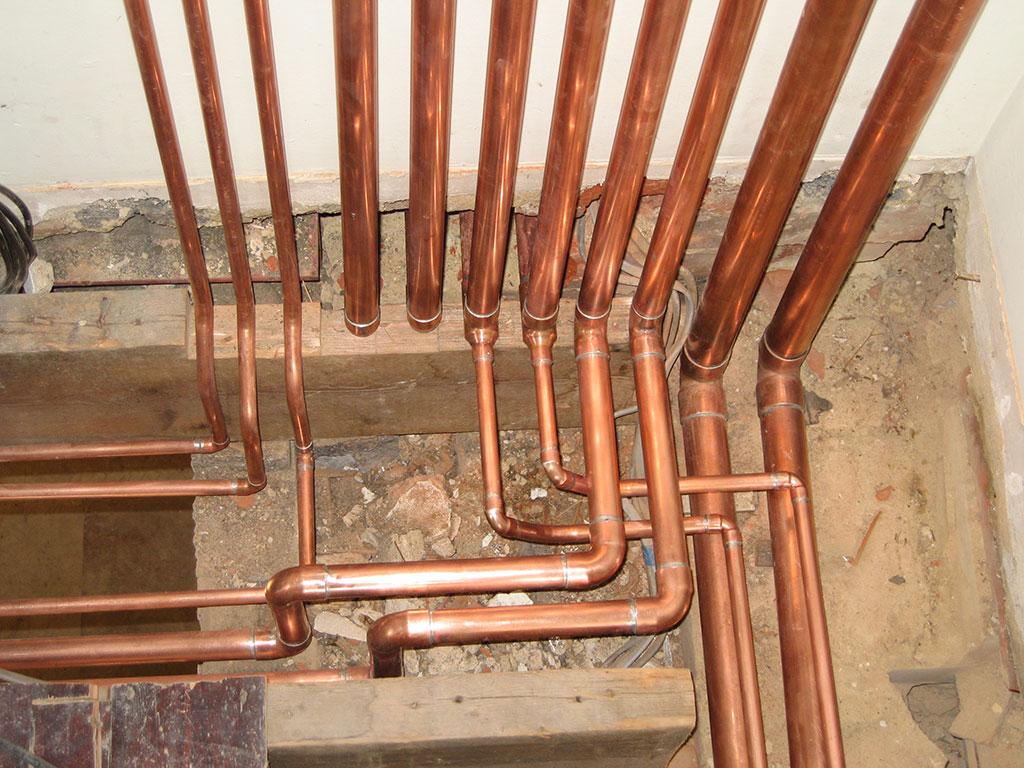 Complex copper pipe assembly — multiple bends and joints rising vertically in a plant area