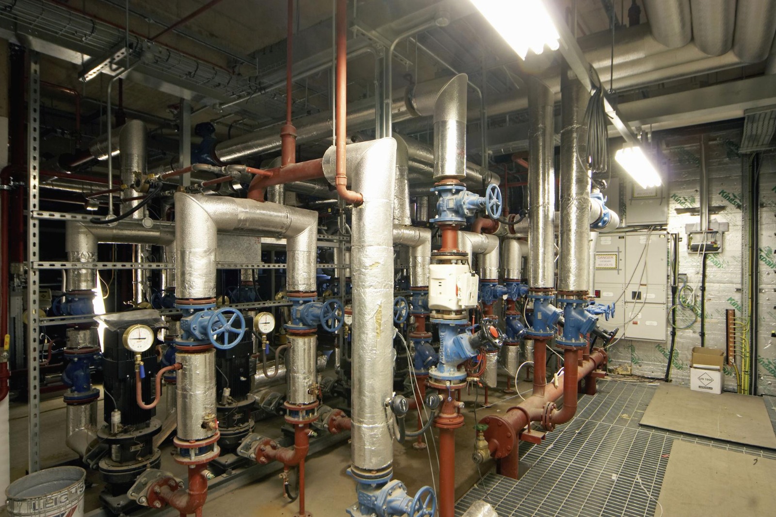 Commercial plant room with large insulated pipework, blue valves, and pressure gauges