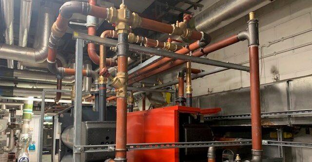 Commercial plant room with copper and steel pipework and a large red heat exchanger unit