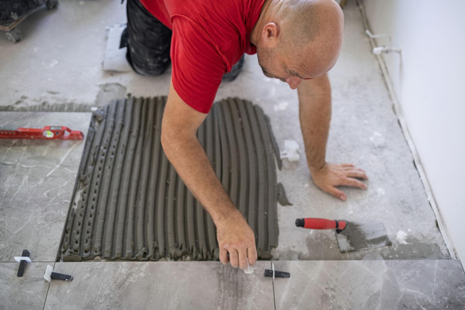 Tiler in red shirt applying notched trowel adhesive for large format floor tile installation
