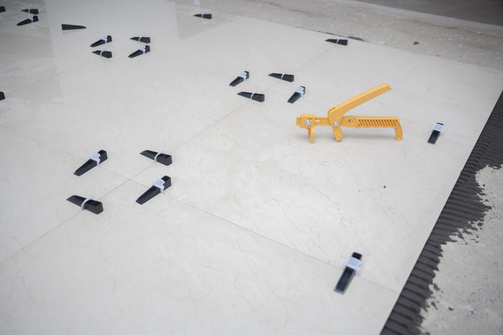 Large white marble-effect floor tiles being set with a levelling clip system and piston gun