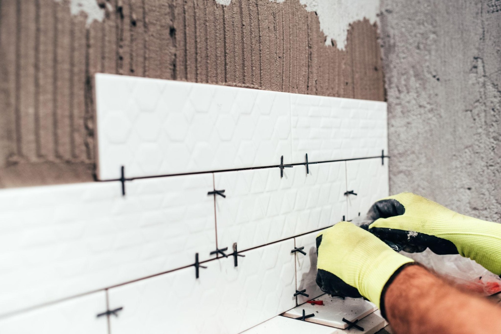 Tiler's hand placing small white 3D brick-effect wall tiles with cross spacers