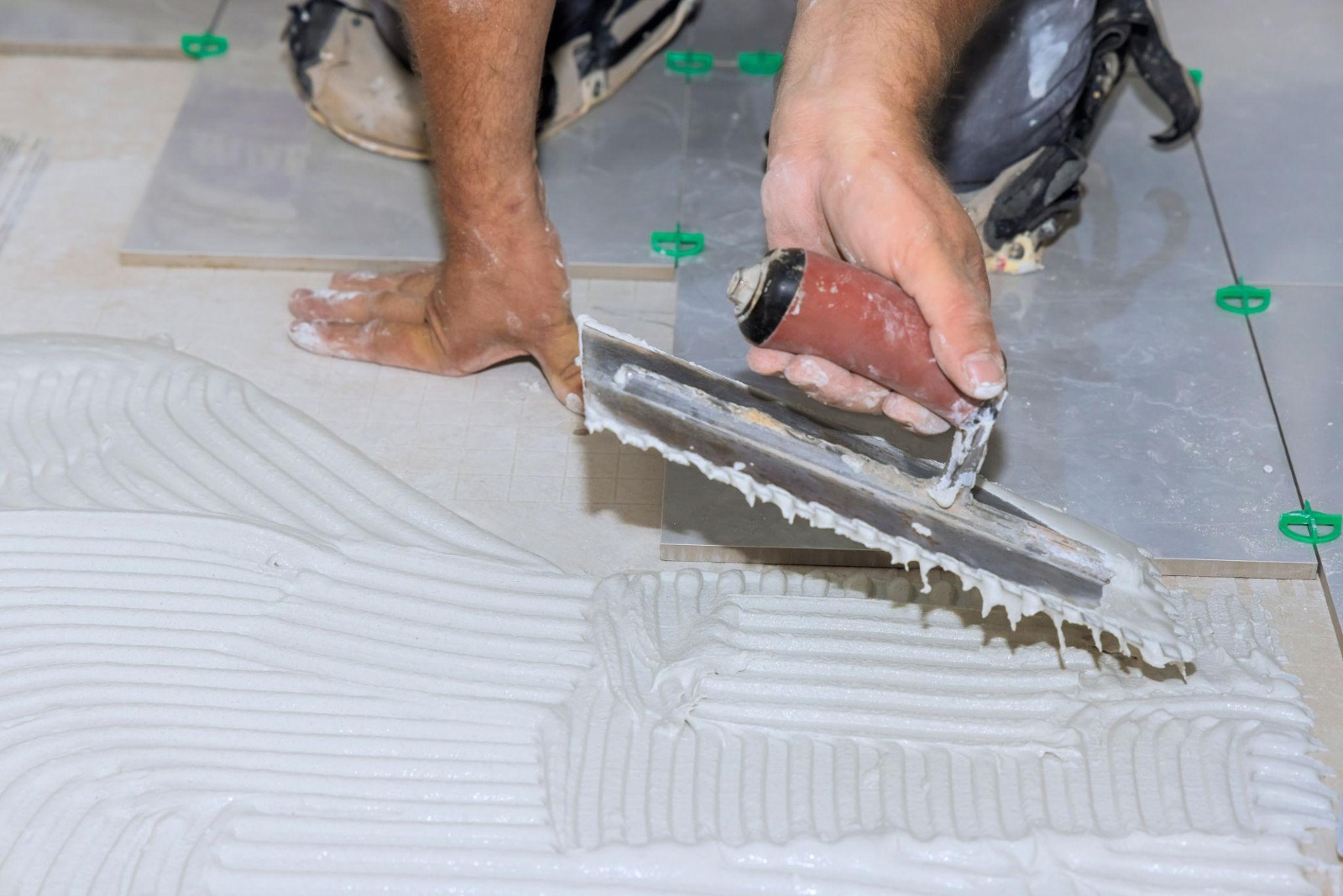 Tiler applying notched trowel adhesive for floor tile installation in progress