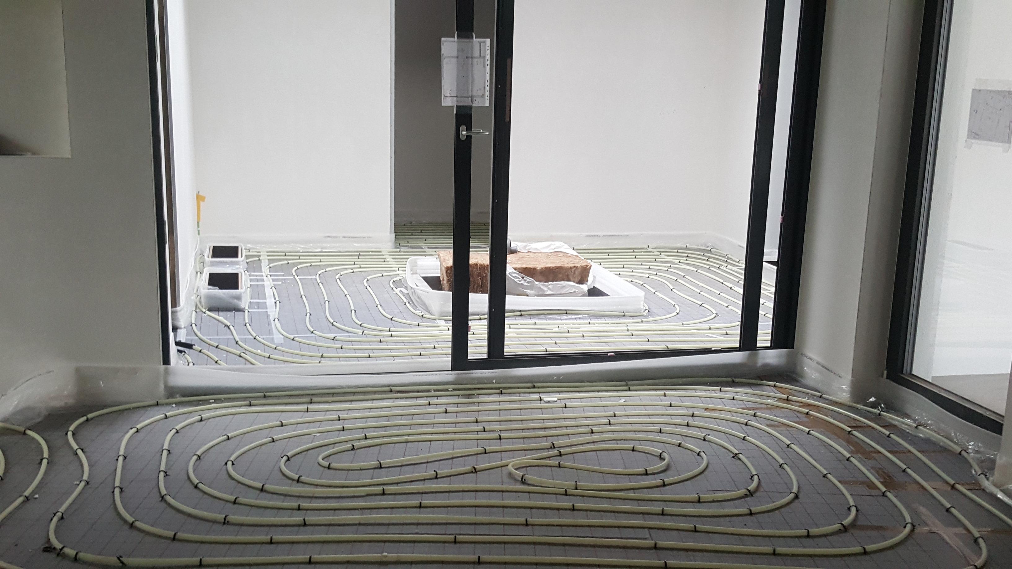 White UFH pipe loops laid on insulation board in a new-build room with patio doors