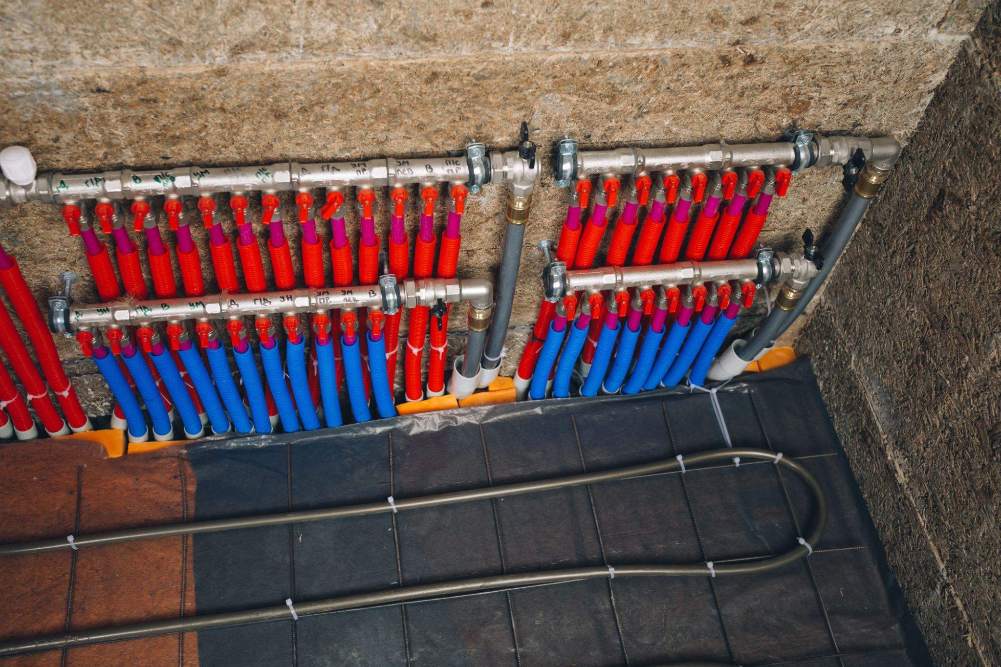 UFH manifold — red and blue colour-coded pipes with Rockwool insulation backing and tile edge visible