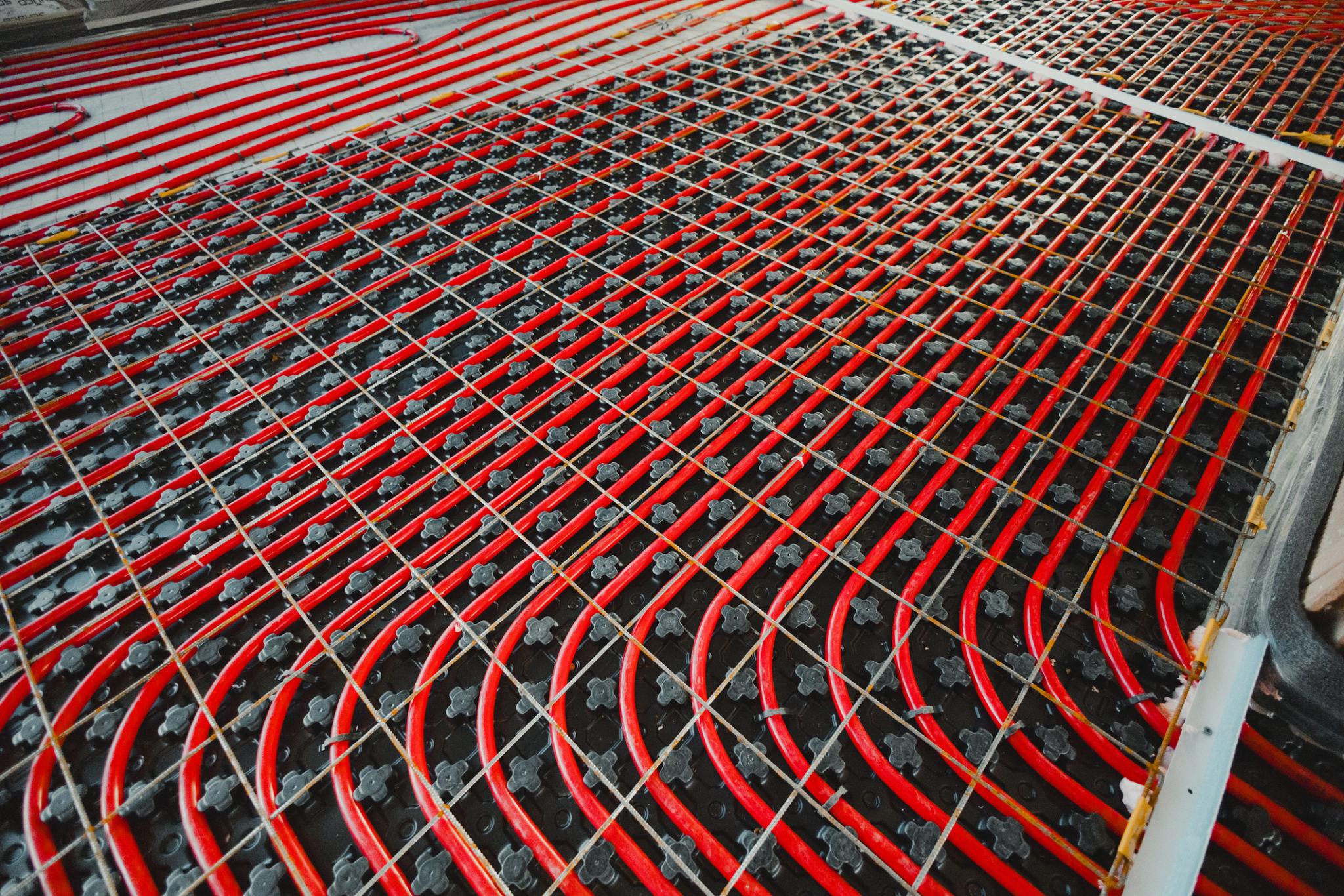 Large commercial floor installation — red UFH pipes laid on black mesh grid