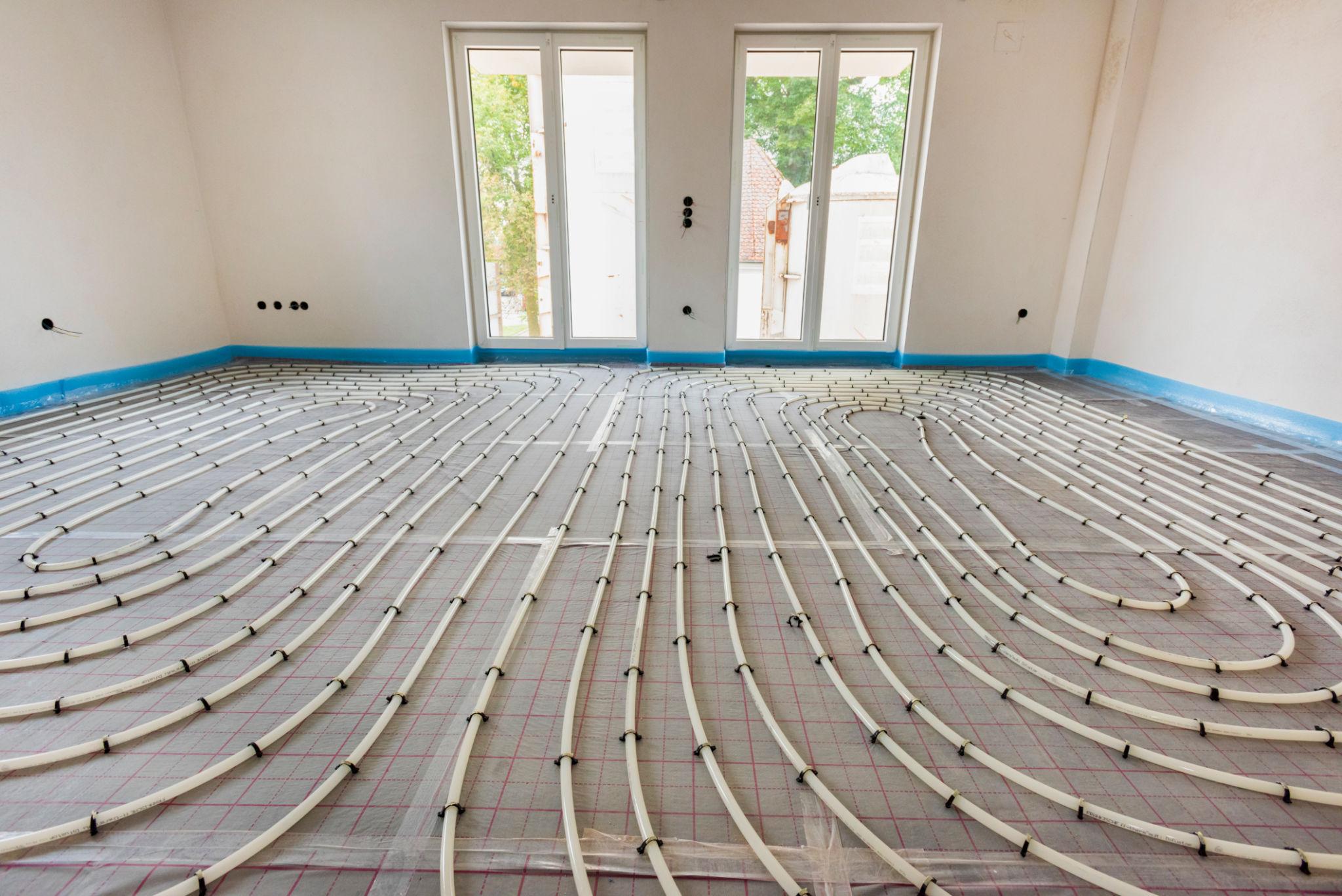White UFH pipe loops in a large empty room — neat serpentine pattern on insulation board