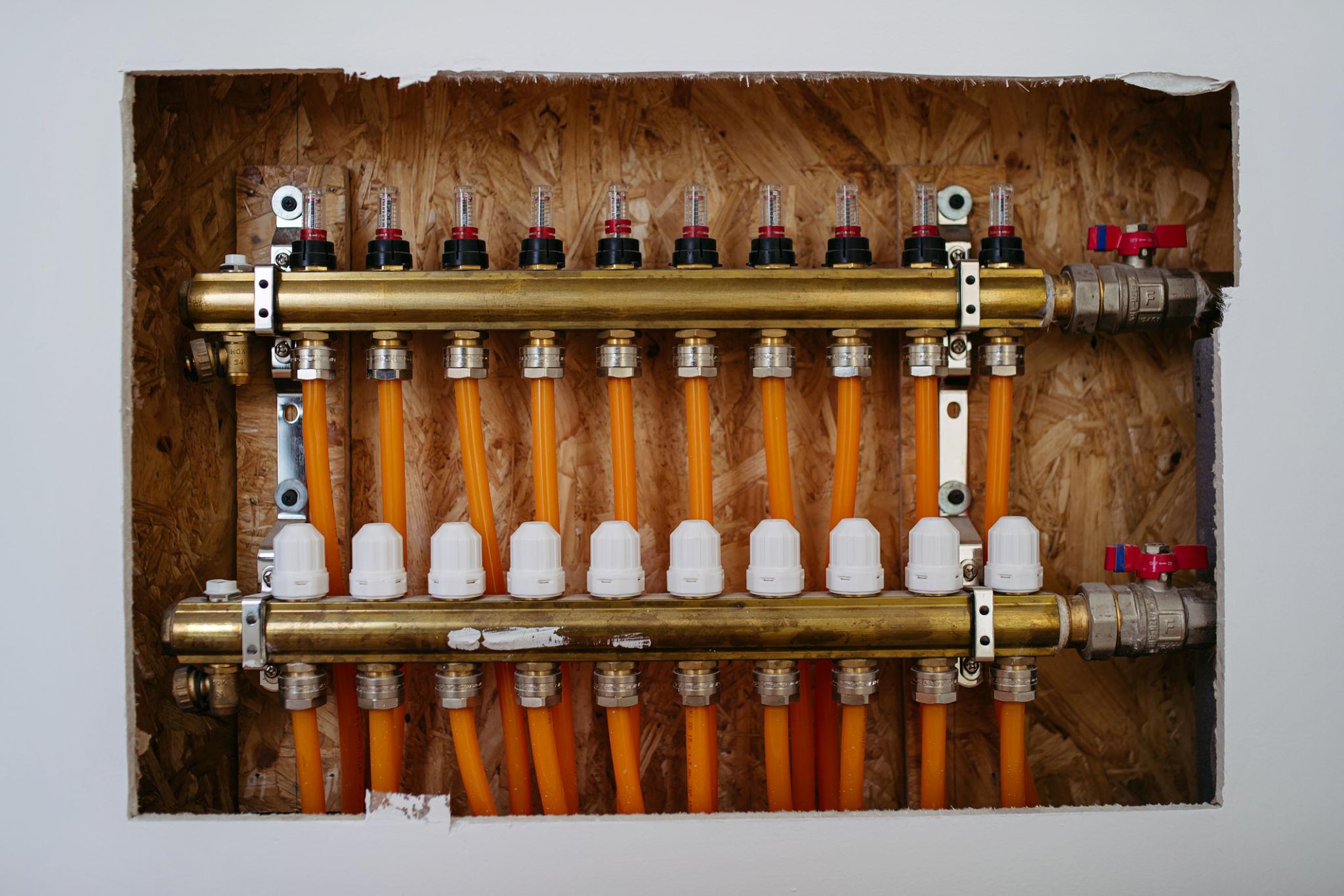 Brass UFH manifold mounted in recessed wall box — orange pipes connected and ready for screed