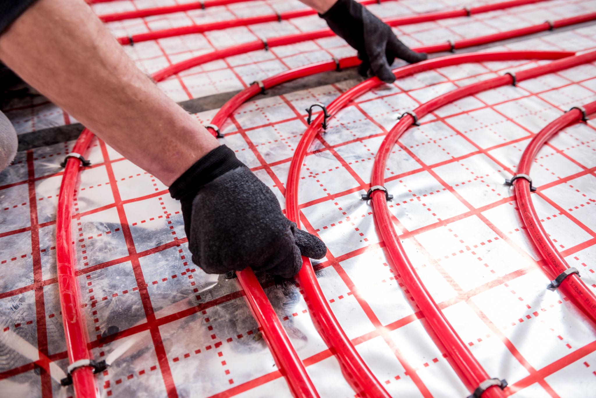 Operative's gloved hands laying red UFH pipe on foil insulation mat