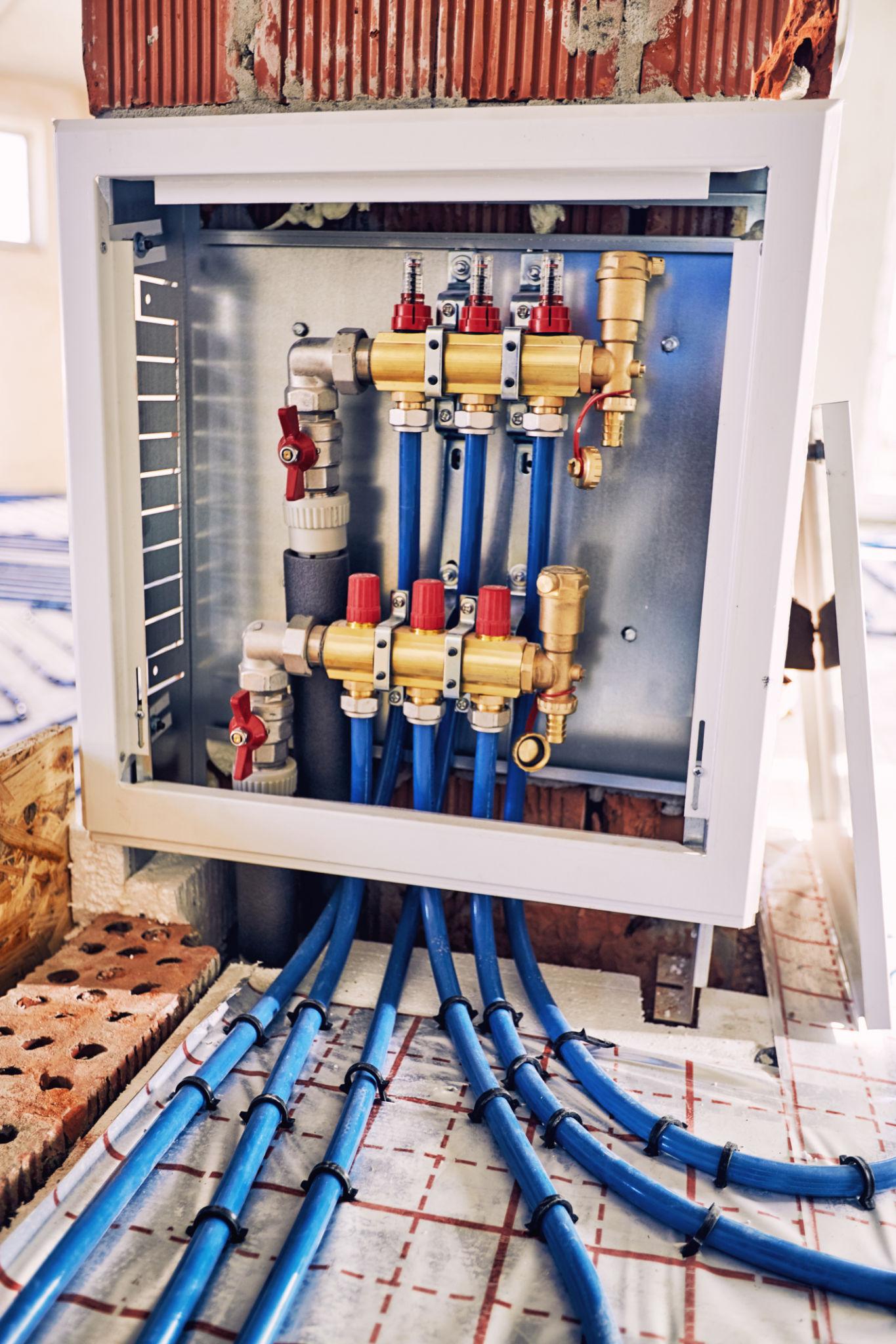 Blue pipe distribution manifold in wall-mounted cabinet — zone circuits running to floor system